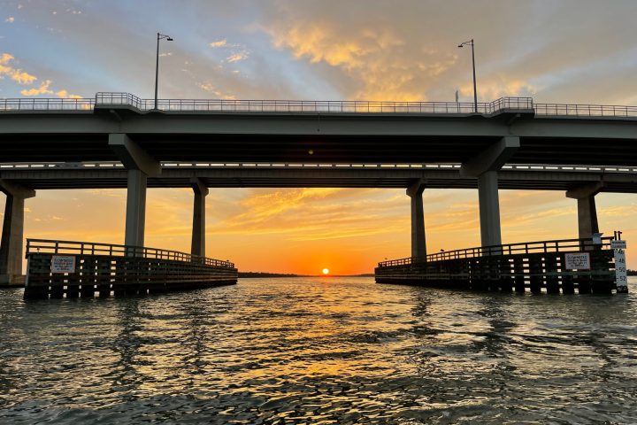 view of a bridge from the water at sunset